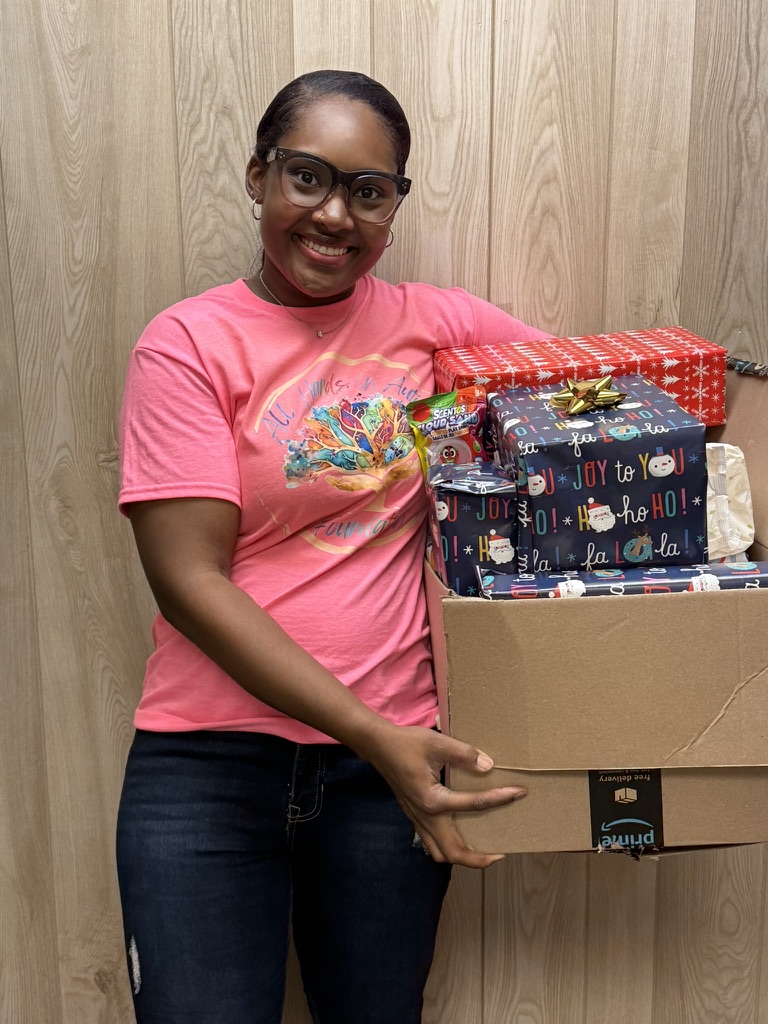 All Hands in Autism Foundation Founder and CEO wearing a pink shirt and holding a large box of wrapped gifts