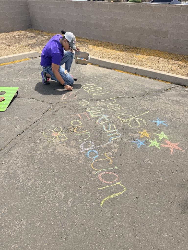 A volunteer writing All Hands in Autism Foundation in colorful sidewalk chalk