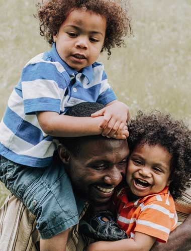 A father smiling while carrying two young children