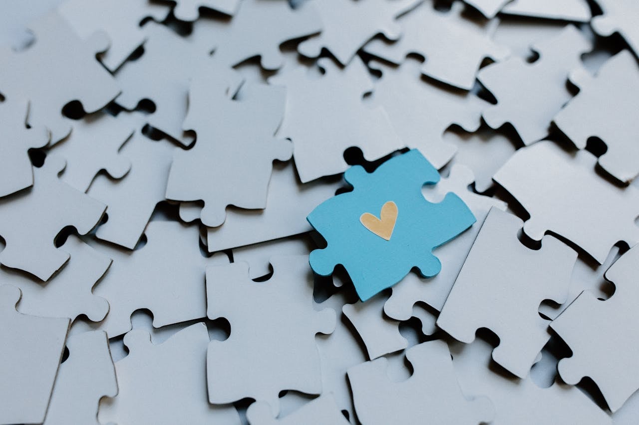 A blue puzzle piece with a heart among white puzzle pieces
